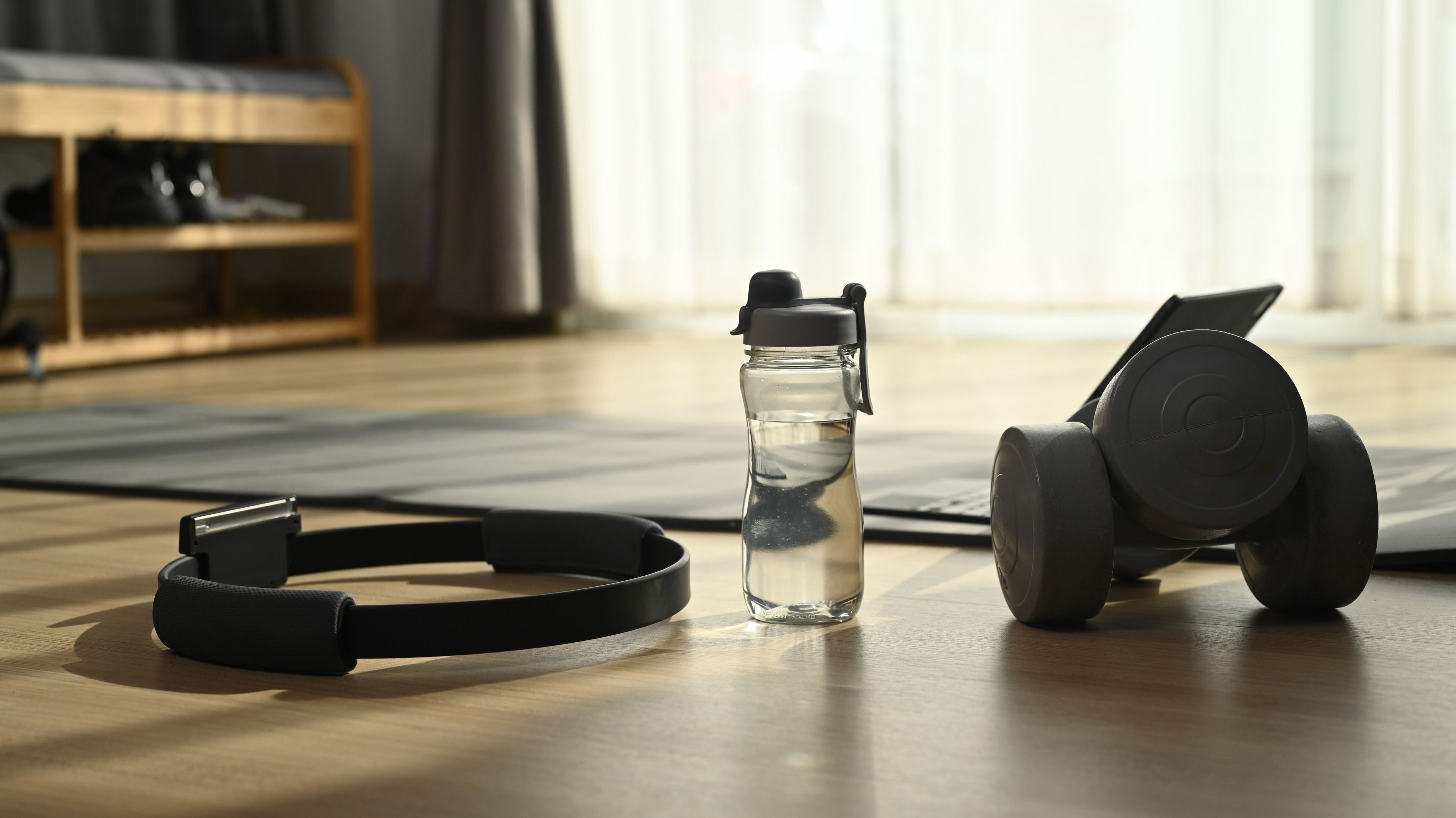 Home workout setup with a water bottle, resistance ring, and dumbbells on a wooden floor.